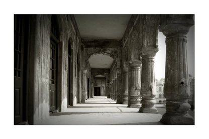 Black and white architectural photograph of a historic corridor with large stone columns and arches, presented as a square print with a white border.