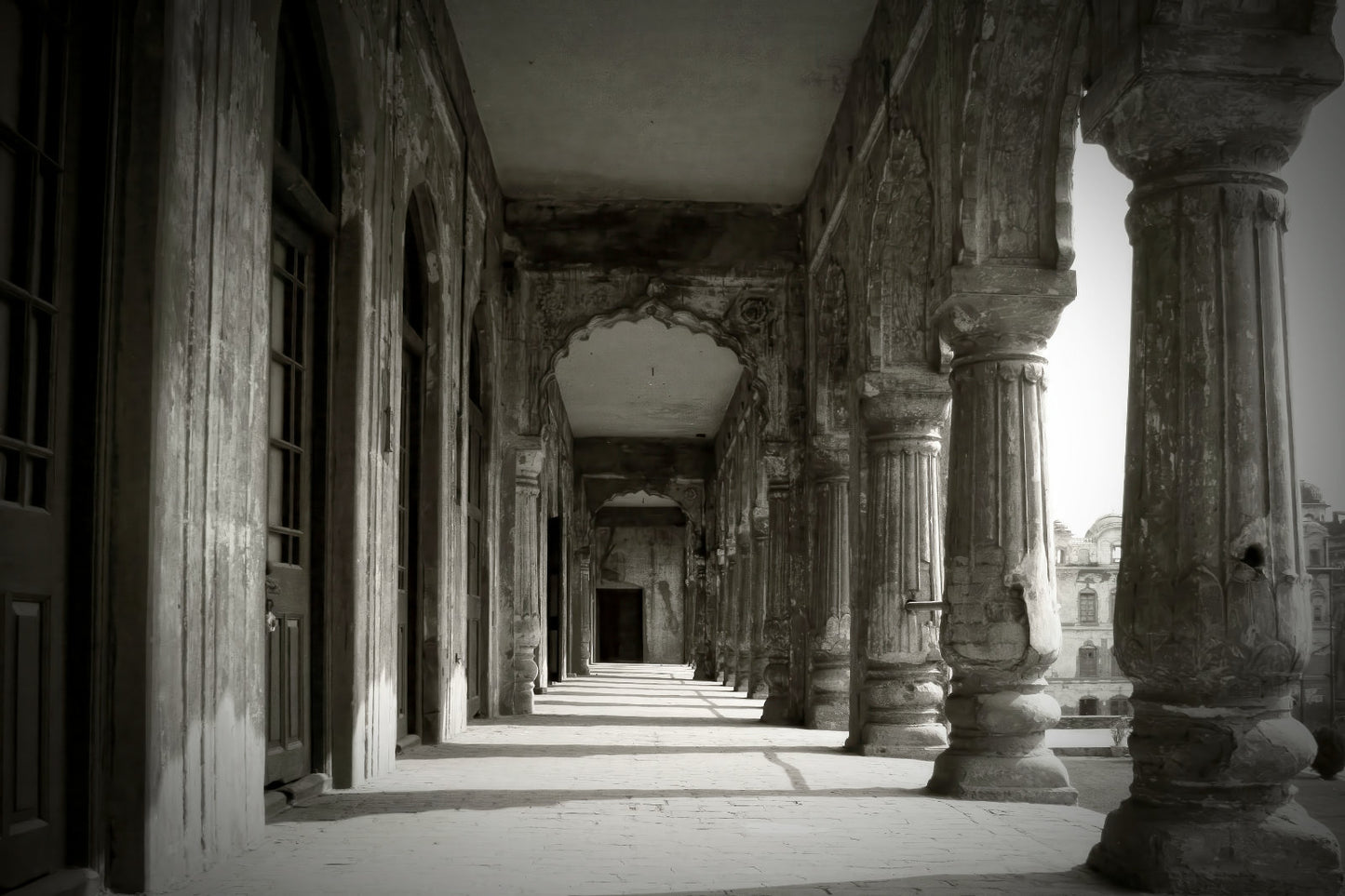 Black and white photograph of an ancient stone colonnade with tall fluted columns and arched passageways receding into the background.