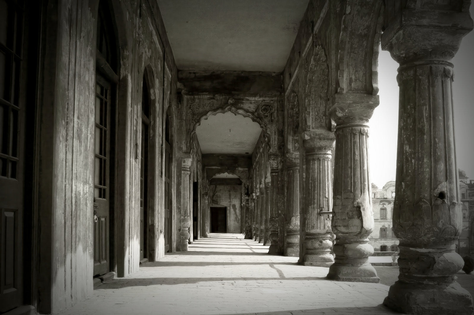 Black and white photograph of an ancient stone colonnade with tall fluted columns and arched passageways receding into the background.