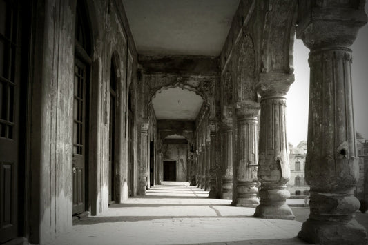Black and white photograph of an ancient stone colonnade with tall fluted columns and arched passageways receding into the background.
