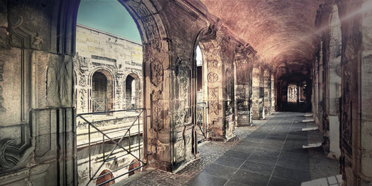 A long stone corridor with arches and carved walls, leading into the distance under a vaulted ceiling in a historic building.