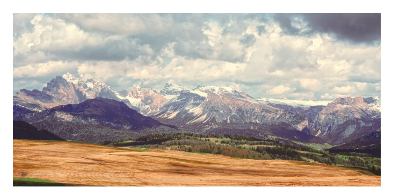 The jagged Dolomites rise beyond golden alpine fields beneath a cloud-filled sky in a photo mount