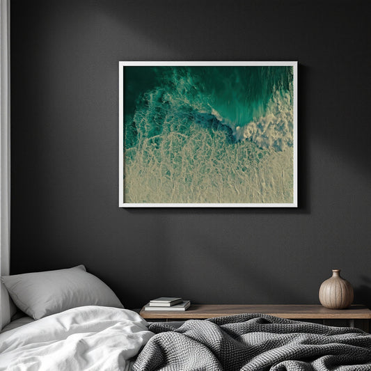 A framed square wall art print showing an abstract ocean wave in teal, turquoise, and cream tones, displayed above a bed in a dark bedroom setting.