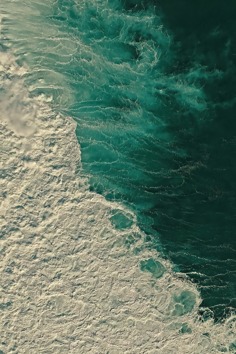 Aerial view of ocean waves with white foam meeting deep teal and dark green water.