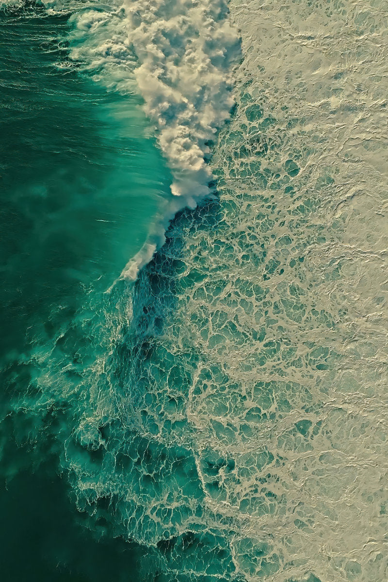 Aerial view of ocean waves with deep teal water on the left and foamy white surf on the right.