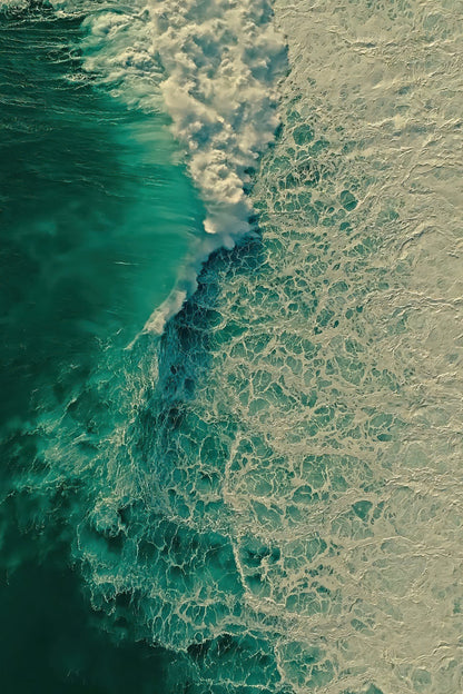 Aerial view of ocean waves with deep teal water on the left and foamy white surf on the right.