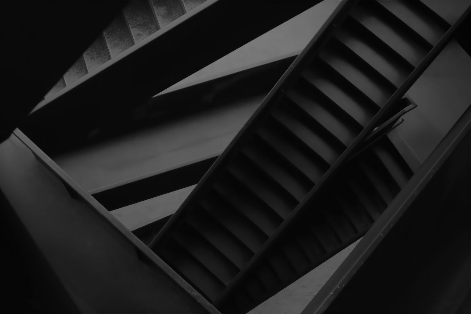 A dramatic black and white photograph of an abstract architectural staircase with diagonal steps and structural beams.