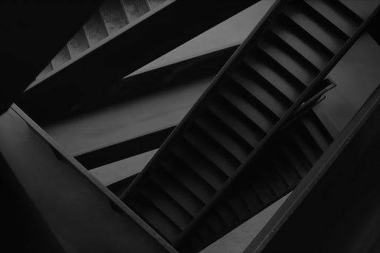 A dramatic black and white photograph of an abstract architectural staircase with diagonal steps and structural beams.