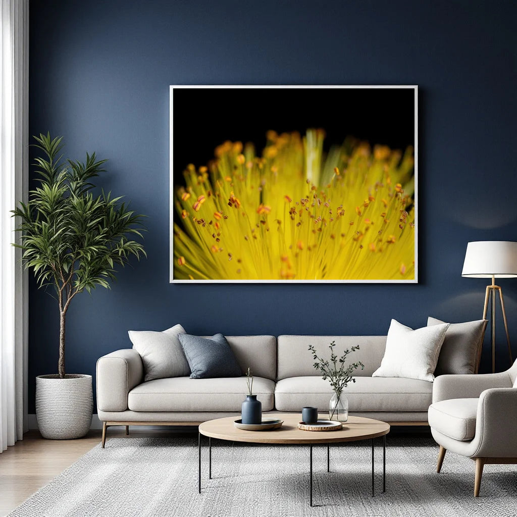 A framed wall art print featuring a close-up yellow flower on a black background, displayed above a light gray sofa in a modern living room with a blue wall, potted plant, coffee table, and floor lamp.