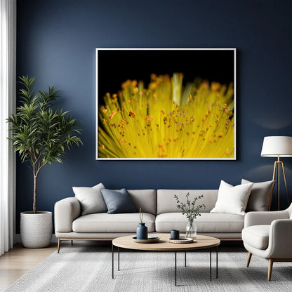 A framed wall art print featuring a close-up yellow flower on a black background, displayed above a light gray sofa in a modern living room with a blue wall, potted plant, coffee table, and floor lamp.