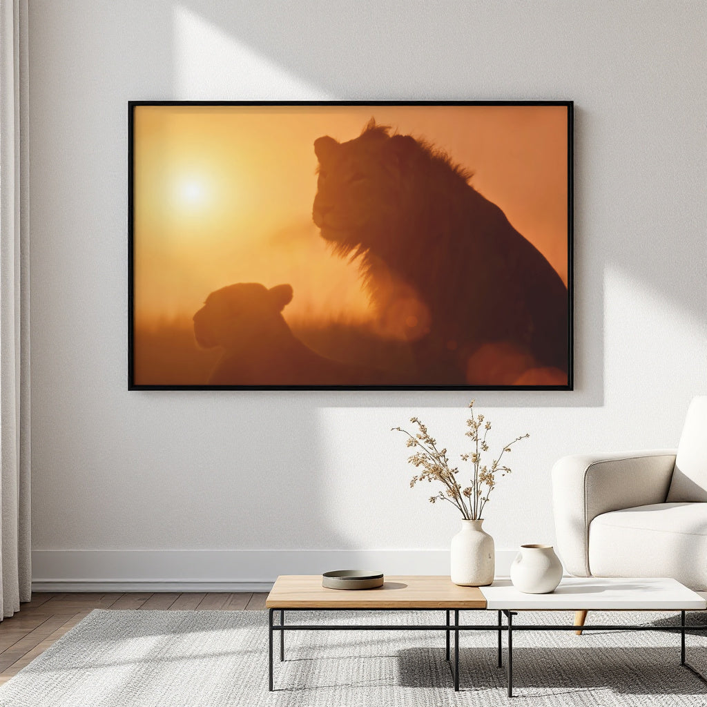 A large framed wall art print showing two lion silhouettes against a warm orange sunset hangs on a white wall above a coffee table in a modern living room setting.