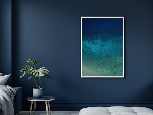 A large framed vertical art print depicting a vibrant blue shades of the ocean , displayed on a dark blue wall in a modern living room.