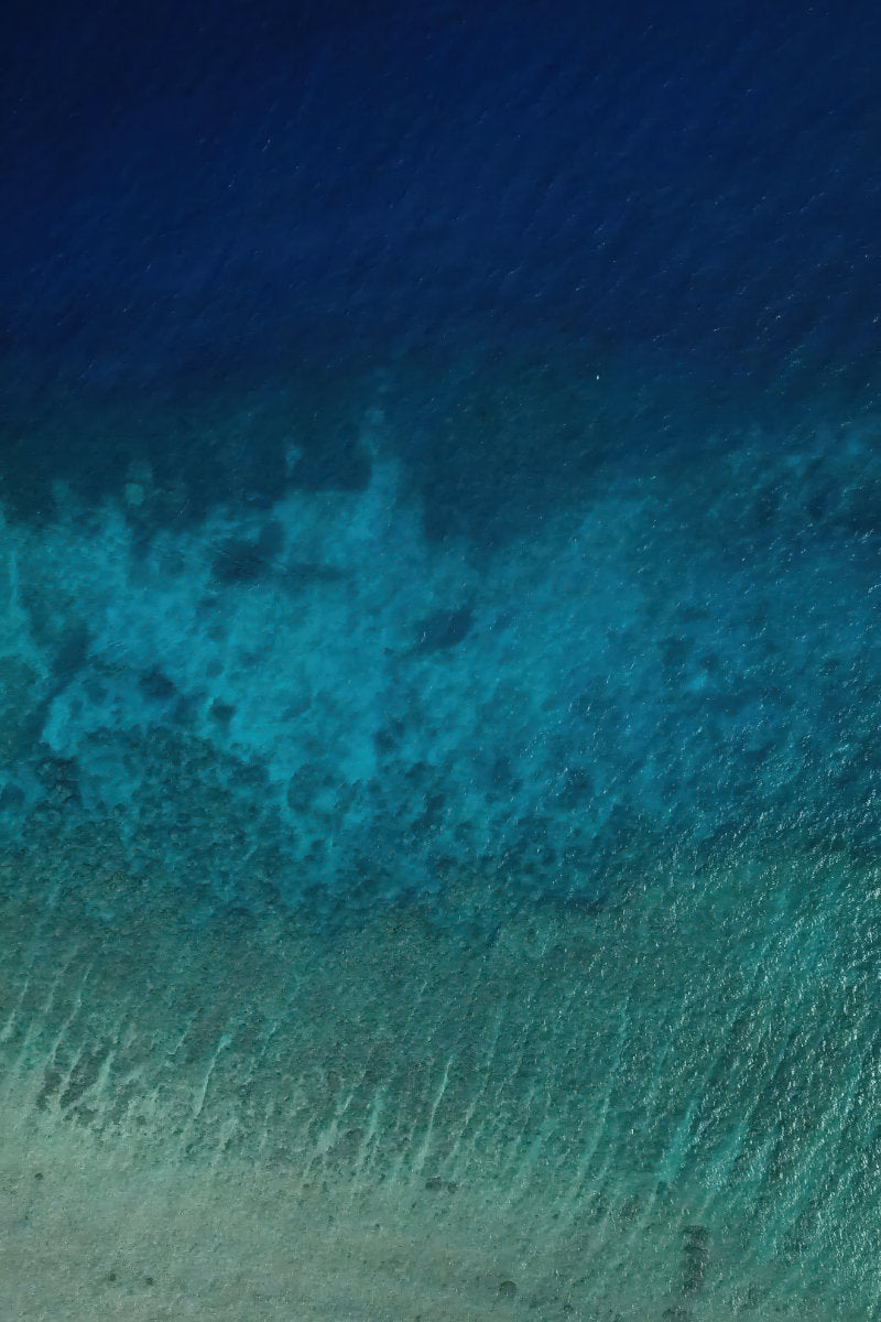 Three distinct bands of blue run across clear ocean water in an aerial view.
