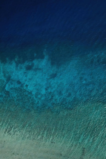 Three distinct bands of blue run across clear ocean water in an aerial view.