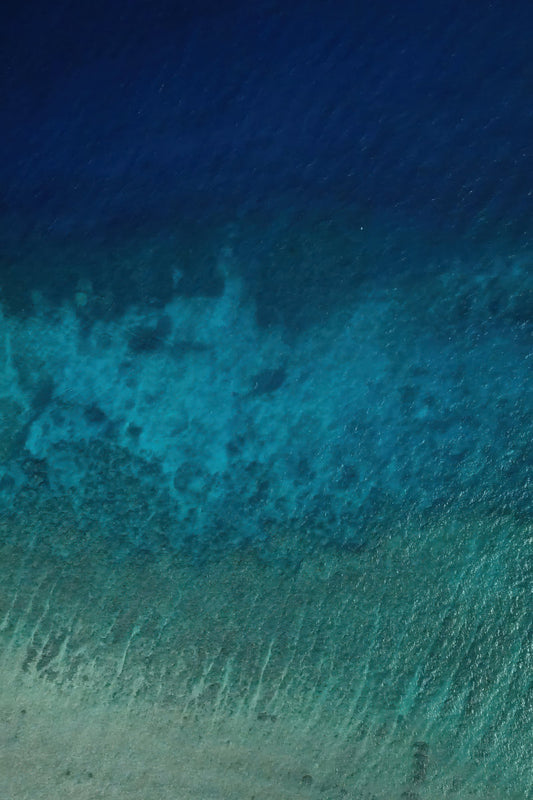 Three distinct bands of blue run across clear ocean water in an aerial view.