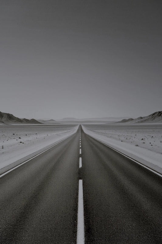 A straight paved road runs through a flat desert landscape under a pale gray sky, with low hills visible on both sides and a dashed white line down the center.