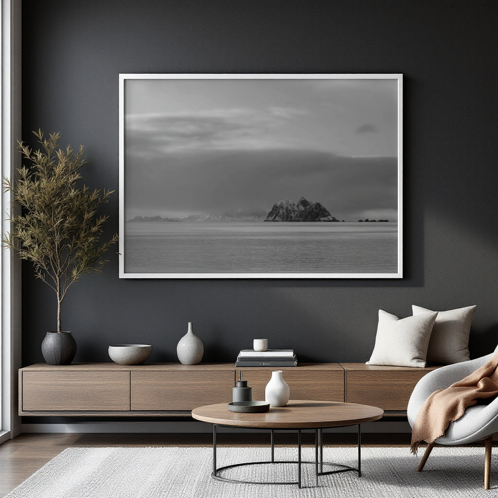 A large black and white framed landscape photograph of a rocky island on the sea, displayed on a dark gray wall in a modern living room setting.
