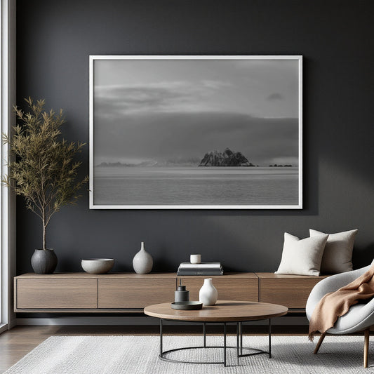 A large black and white framed landscape photograph of a rocky island on the sea, displayed on a dark gray wall in a modern living room setting.