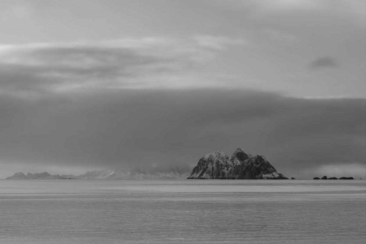 Monochrome photo of small rock island in the calm ocean. 
