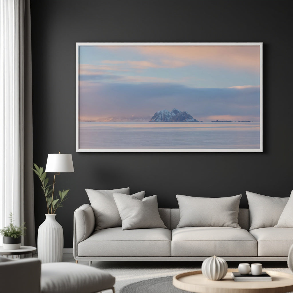 A large framed landscape art print of a snowy mountain island under a pastel sunset sky, displayed on a dark charcoal wall above a modern light gray sofa in a styled living room.