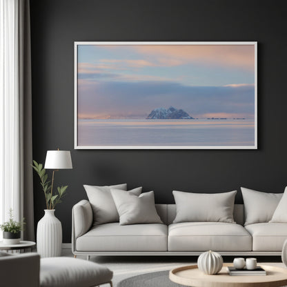A large framed landscape art print of a snowy mountain island under a pastel sunset sky, displayed on a dark charcoal wall above a modern light gray sofa in a styled living room.
