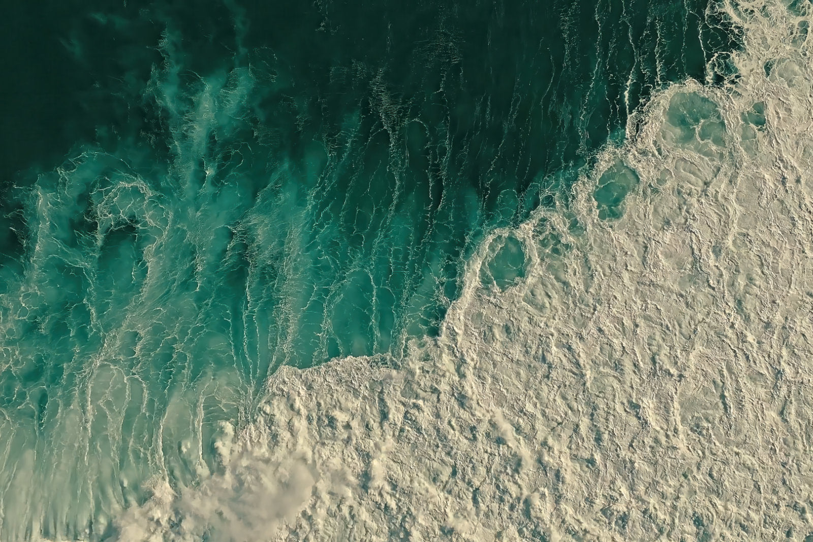 Aerial view of ocean waves with deep teal water transitioning into white sea foam.