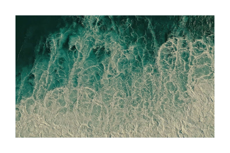 An aerial photograph of ocean waves with swirling turquoise water and white foam, presented as a square art print with a white border.