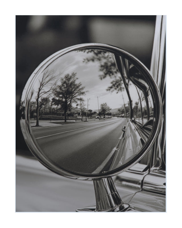 A black and white art print depicting a classic car side-view mirror reflecting a tree-lined road.