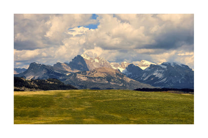 A scenic landscape photograph of rugged snow-capped mountains under a dramatic cloudy sky, with a green valley in the foreground, shown as a square print centered on a white background.