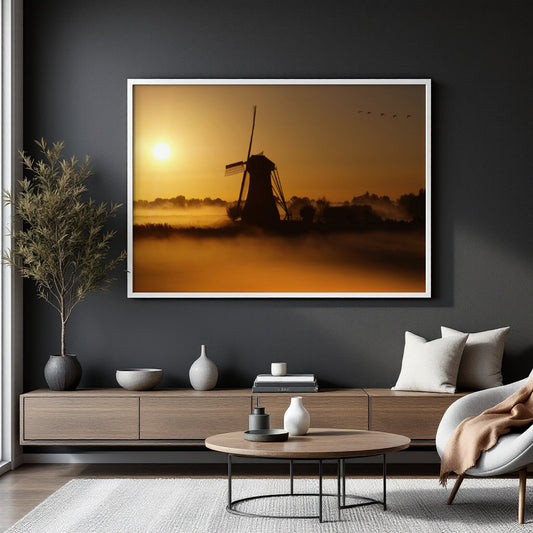 A large framed wall art print depicting a windmill silhouette at sunrise or sunset over a misty landscape, displayed on a dark gray wall above a modern wooden console and coffee table in a styled living room.