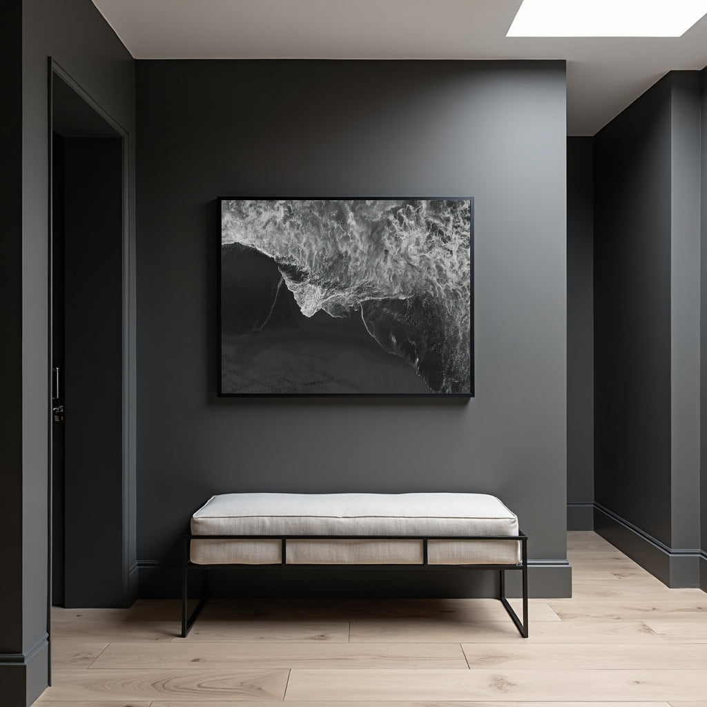 A black and white abstract framed wall art print hangs on a dark gray entryway wall above a light beige upholstered bench with black metal legs, set on light wood flooring.