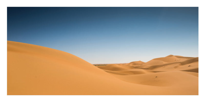 A scenic landscape photograph of rolling golden sand dunes under a clear blue sky, presented with a white border.
