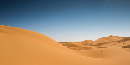 A scenic landscape photograph of rolling golden sand dunes under a clear blue sky.