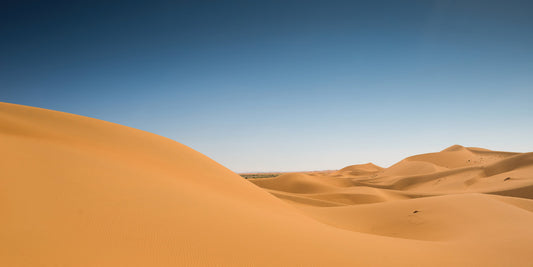 A scenic landscape photograph of rolling golden sand dunes under a clear blue sky.