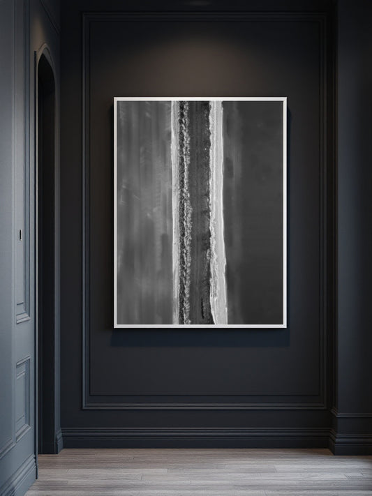 A framed abstract black and white vertical art print hanging on a dark charcoal paneled wall above light wood flooring.