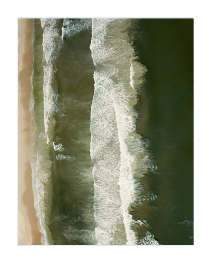 An aerial photograph of ocean waves rolling onto a sandy beach, presented as a vertical art print with a white border.