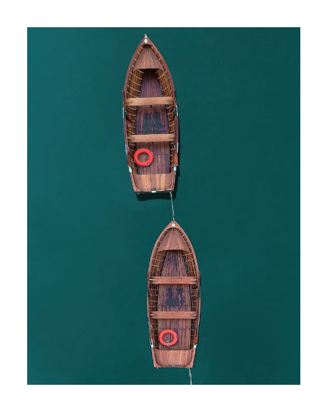 An aerial view of two wooden rowboats floating on deep teal water, with red life preservers in each boat.