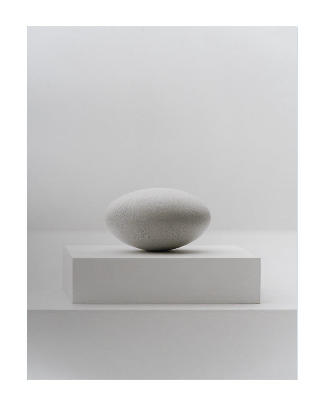A minimalist studio shot of a smooth, matte gray stone sculpture resting on a matching rectangular pedestal against a clean, light gray background.