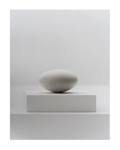 A minimalist studio shot of a smooth, matte gray stone sculpture resting on a matching rectangular pedestal against a clean, light gray background.