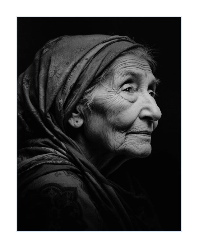Black and white portrait photograph of an elderly woman in profile wearing a patterned headscarf, presented as wall art with a white border.
