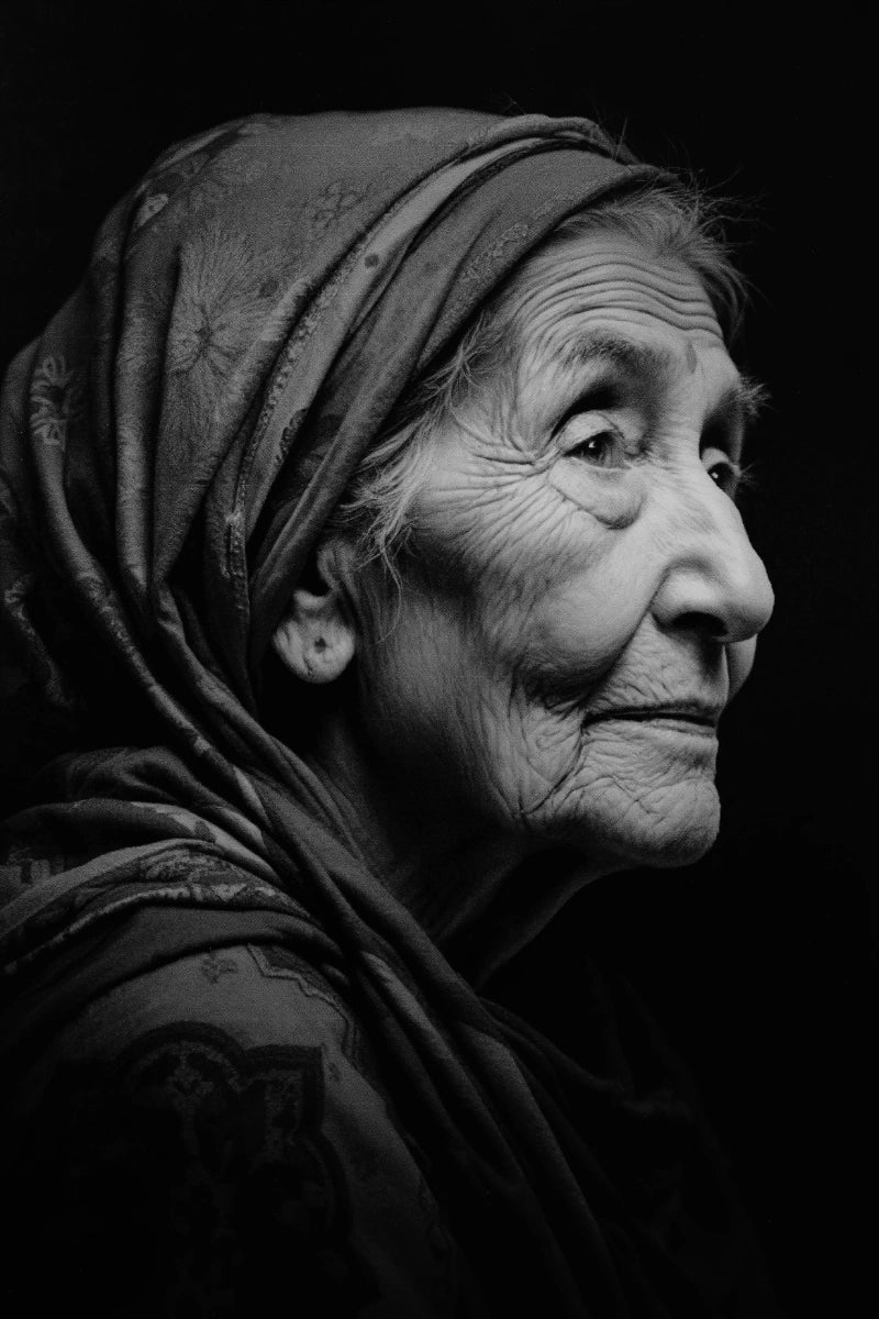 Black and white close-up portrait of an elderly woman in profile wearing a patterned headscarf against a dark background.