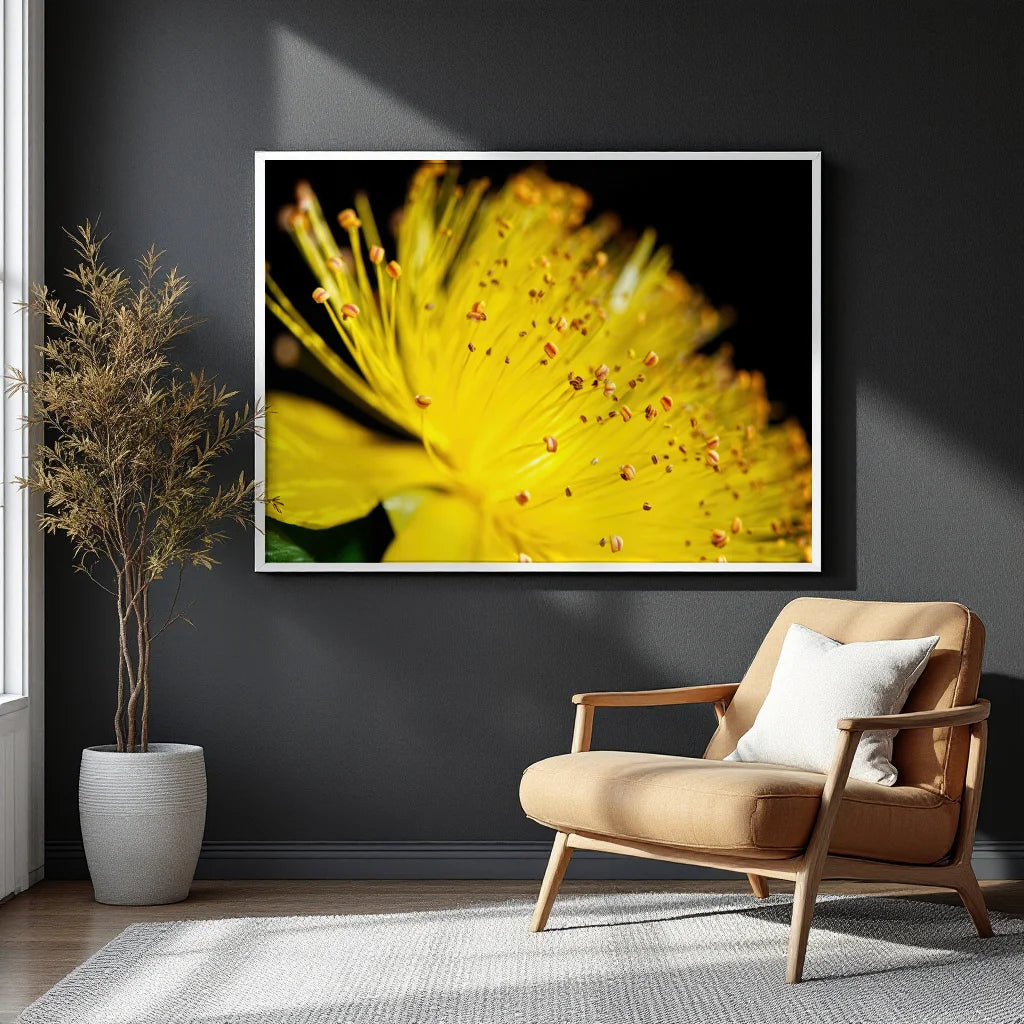 A framed wall art print featuring a close-up yellow flower on a black background, displayed above a tan armchair in a modern room with a dark gray wall, potted plant, and white rug.