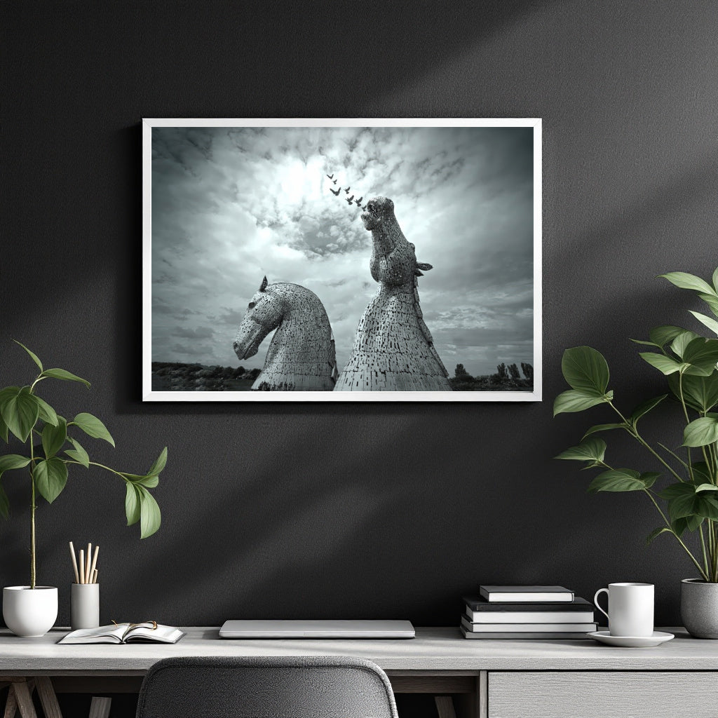 A framed black and white art print depicting the Kullreid Horse statues at Edinburgh, displayed on a dark gray wall above a styled desk with plants and office accessories.