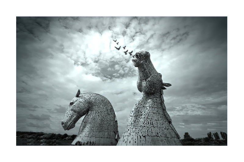 Black and white fine art photograph of the Kiptik horse sculptures at the Tate Modern in London, featuring two large horse heads made of woven steel and netting under a dramatic cloudy sky with a flock of birds flying above.