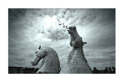 Black and white fine art photograph of the Kiptik horse sculptures at the Tate Modern in London, featuring two large horse heads made of woven steel and netting under a dramatic cloudy sky with a flock of birds flying above.
