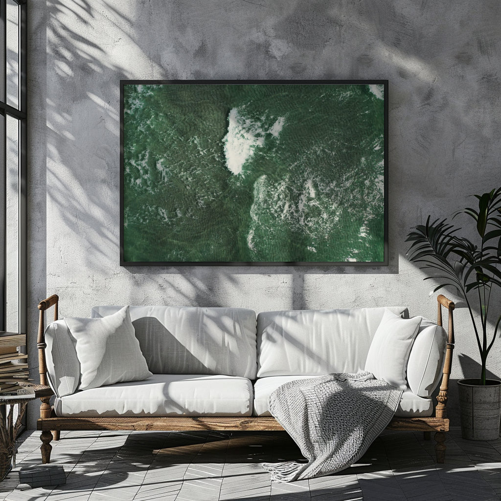A large framed wall art print featuring a green and white aerial landscape is displayed above a white sofa in a modern, sunlit living room with a concrete wall and potted plant.