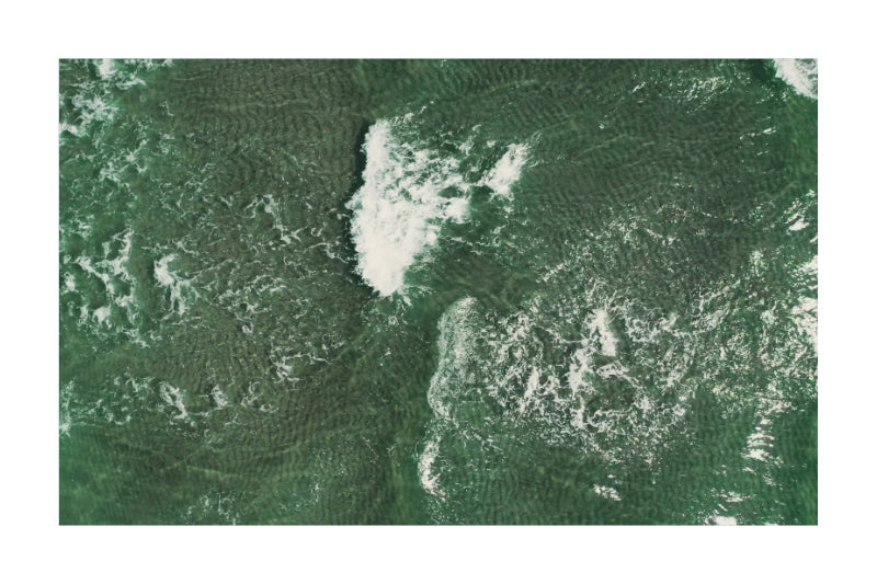 A square art print or photograph showing an aerial view of green water with white foam and ripple patterns, presented on a white background with a thin gray border.