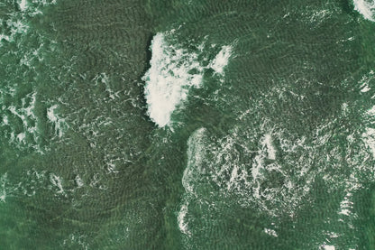 Aerial view of a green river or stream with white rushing water and textured rippling surface.