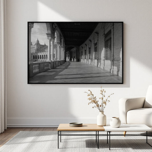 A large black and white framed wall art print depicting a long architectural corridor, displayed on a light wall above a coffee table in a modern living room setting.