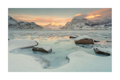 A scenic winter landscape print showing snow-covered rocks in a partially frozen icy body of water, with mountains and a soft sunset sky in the background.